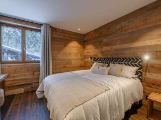 Experience cozy mountain living in this charming bedroom, featuring rustic wood-paneled walls and a comfortable bed adorned with plush pillows.