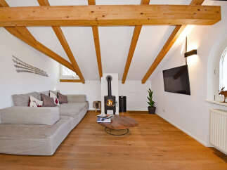 Experience cozy living in this charming attic apartment, featuring exposed wooden beams and a modern wood-burning stove.