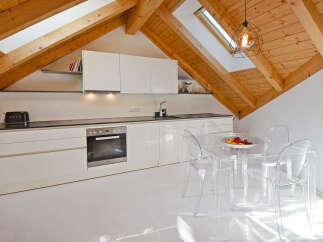 Discover this modern attic kitchen featuring sleek white cabinetry and a built-in oven, complemented by a stylish glass dining set.