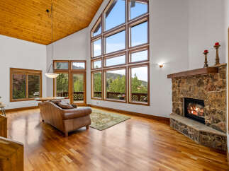 Experience breathtaking mountain views from this stunning living room, featuring a grand stone fireplace and soaring vaulted ceilings with exposed wood beams.