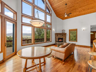 Experience breathtaking mountain views from this stunning living room, featuring a grand stone fireplace and soaring vaulted ceilings with exposed wood beams.