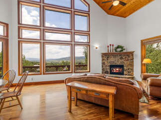 Experience breathtaking mountain views from this stunning living room, featuring a grand stone fireplace and expansive windows that flood the space with natural light.