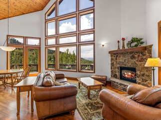 Experience breathtaking mountain views from this stunning living room, featuring a grand stone fireplace and soaring vaulted ceilings with exposed wood beams.