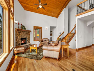 Experience rustic elegance in this spacious living room featuring a grand stone fireplace and soaring vaulted ceilings with rich wood accents.