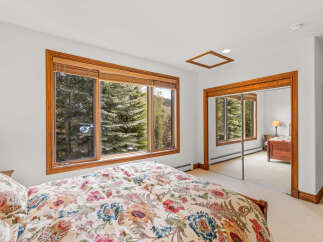 Experience serene mountain living in this charming bedroom, featuring a large window with breathtaking views of lush trees and a distant lake.