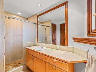 This bathroom features a spacious walk-in shower with tiled walls and a glass door, complemented by a large vanity with ample counter space and wooden cabinetry.