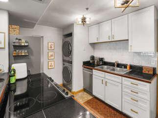 Discover this charming kitchen featuring sleek white cabinetry with modern gold hardware, complemented by a black granite countertop and a stylish tile backsplash.