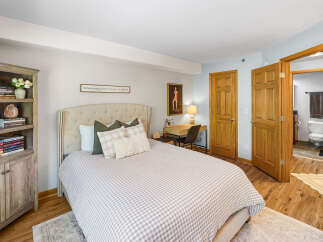 This charming bedroom features a comfortable tufted headboard bed with a classic gingham duvet, complemented by a rustic wooden bookshelf filled with decorative items and books.