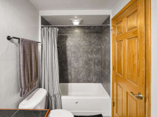 This bathroom features a clean white bathtub with a dark tiled shower surround and a striped shower curtain.