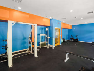 This vibrant gym features a full range of Cybex equipment, including a squat rack with weight plates and a cable crossover machine.