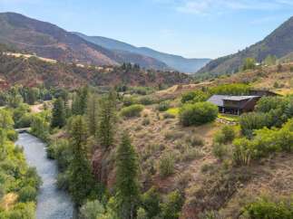 Nestled in a picturesque mountain valley, this stunning property offers a serene retreat with a modern home featuring a distinctive angular roofline and large windows.