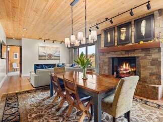Experience rustic elegance in this spacious living and dining area, featuring a magnificent stone fireplace and a warm, wood-paneled ceiling.