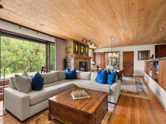 Experience rustic elegance in this spacious living area, featuring a large sectional sofa adorned with vibrant blue pillows, centered around a rustic wooden coffee table with a chess set.