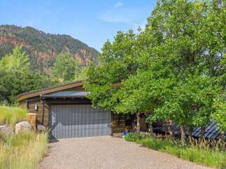 Nestled against a backdrop of majestic mountains, this modern home offers a unique architectural design with a striking corrugated metal garage door.