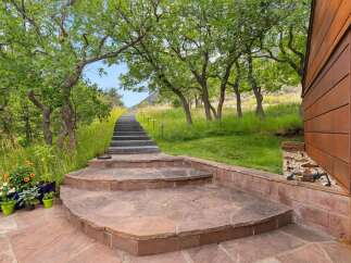Ascend a scenic pathway lined with mature trees and lush greenery, leading to a modern home with striking rusted metal siding.