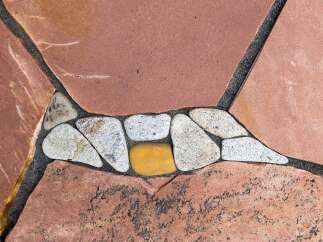 Enhance your outdoor living space with this unique flagstone pathway, featuring a decorative inlay of smooth river stones and a striking yellow accent stone.