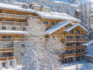 Experience luxury mountain living in this stunning chalet, featuring a rustic wooden exterior and stone accents, perfect for a winter getaway.