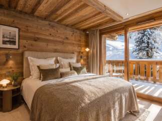 Experience ultimate comfort in this luxurious mountain retreat, featuring a cozy bedroom with a plush bed and stunning panoramic views of snow-covered peaks.