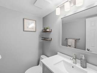 This modern bathroom features a sleek vanity with a white countertop and a brushed nickel faucet, complemented by a large mirror reflecting a towel rack with decorative towels.