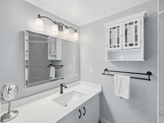 This modern bathroom features a sleek vanity with a white countertop and a dark faucet, complemented by a large, decorative mirror.