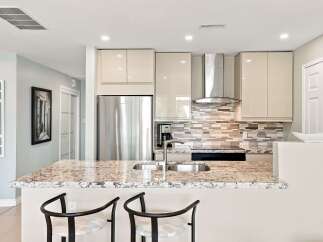 Experience modern luxury in this stunning kitchen, featuring sleek, high-gloss cabinetry and a spacious granite island with a double sink.