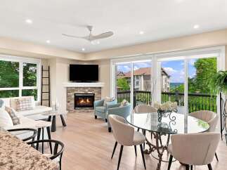 Experience breathtaking lake views from this stunning living and dining area, featuring a modern sectional sofa, a cozy fireplace, and a chic glass-top dining table perfect for entertaining.