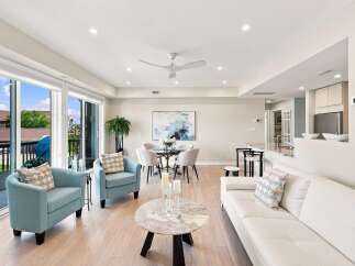 Experience modern living in this bright and airy open-concept space, featuring a comfortable living area with a plush white sofa and two serene blue accent chairs.