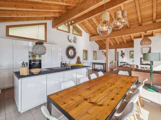 Experience modern alpine living in this stunning open-concept home featuring a sleek white kitchen with a large island and a rustic wooden dining table.