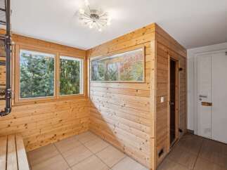 Experience ultimate relaxation in this beautifully appointed sauna room, featuring natural wood paneling and a large window offering serene views of lush greenery.