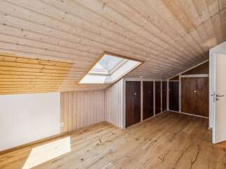 Discover this charming attic room featuring a sloped, wood-paneled ceiling with a central skylight that floods the space with natural light.