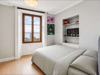 This charming bedroom features a large wooden-framed window offering picturesque views of the water and cityscape.