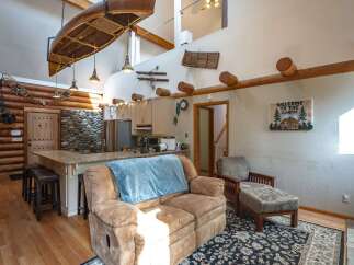 Experience rustic charm in this spacious cabin-style living area, featuring a stunning log interior and a unique canoe suspended from the ceiling.