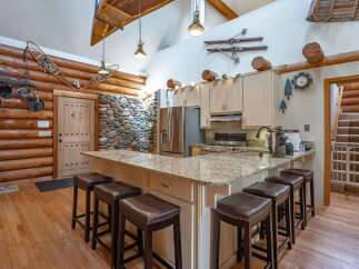 Experience rustic charm in this log cabin kitchen, featuring a spacious granite island with comfortable seating, perfect for casual dining or entertaining.