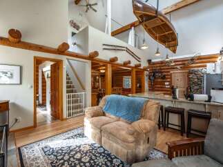 Experience rustic charm in this spacious log cabin living area, featuring a soaring vaulted ceiling with a suspended canoe and exposed wooden beams.
