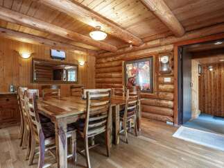 Experience rustic charm in this log cabin dining room, featuring a substantial wooden table surrounded by six chairs, perfect for intimate gatherings.