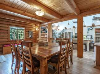 Experience rustic charm in this stunning log home, featuring a spacious dining area with a large wooden table and chairs, perfect for family gatherings.