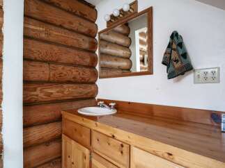 This rustic bathroom features a charming log cabin aesthetic, complete with exposed wooden beams and a warm, natural wood vanity.
