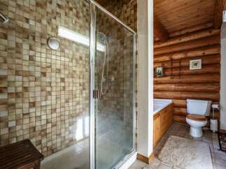 Experience rustic charm in this unique bathroom featuring a tiled shower stall with a wooden bench and a separate bathtub.