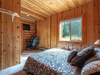 Experience rustic charm in this cozy cabin bedroom, featuring warm wood paneling and a comfortable bed with a nature-inspired duvet.