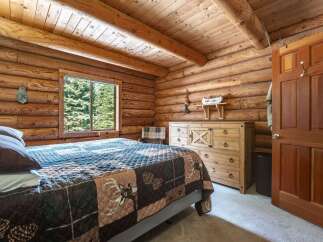 Experience rustic charm in this cozy log cabin bedroom, featuring a comfortable bed adorned with a nature-themed quilt.