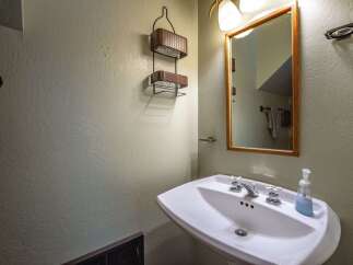 This charming bathroom features a pedestal sink with classic chrome fixtures, complemented by a wooden framed mirror and a decorative wall shelf.