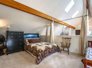 Discover this charming bedroom featuring a cozy quilt-covered bed, a tall black dresser, and a vintage wooden chair.