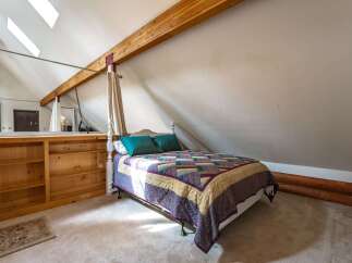 Discover a unique loft bedroom featuring a charming four-poster bed adorned with a colorful quilt and plush teal pillows.