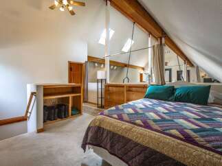 Discover this charming attic bedroom featuring a cozy bed with a vibrant quilt and two plush teal pillows.