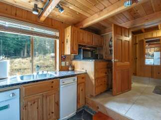 Experience rustic charm in this cozy cabin kitchen, featuring warm wood paneling and a spacious double sink overlooking a serene forest view.