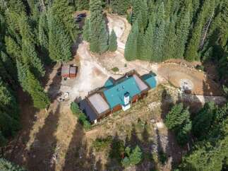 Nestled amidst a dense forest, this property offers a serene retreat with a spacious wooden home featuring a distinctive teal roof and multiple decks.