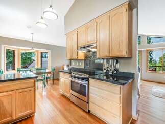 This spacious kitchen boasts light wood cabinetry and sleek black granite countertops, offering ample storage and workspace.
