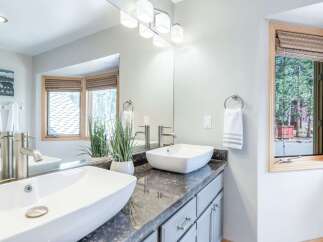 This modern bathroom features a dual vanity with vessel sinks and sleek chrome faucets, complemented by a granite countertop and light gray cabinetry.