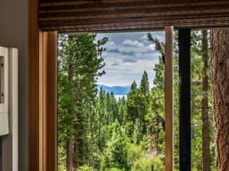 Experience breathtaking lake and mountain views from this stunning property, framed by a lush forest of mature pine trees.