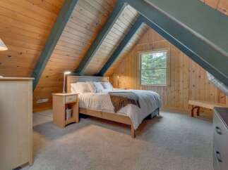 Experience cozy cabin living in this charming attic bedroom, featuring warm wood paneling and exposed beams.